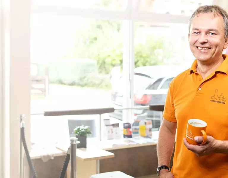 Lächelnder Mann von der Kaffeeküste Laboe mit Kaffeetasse in der Hand