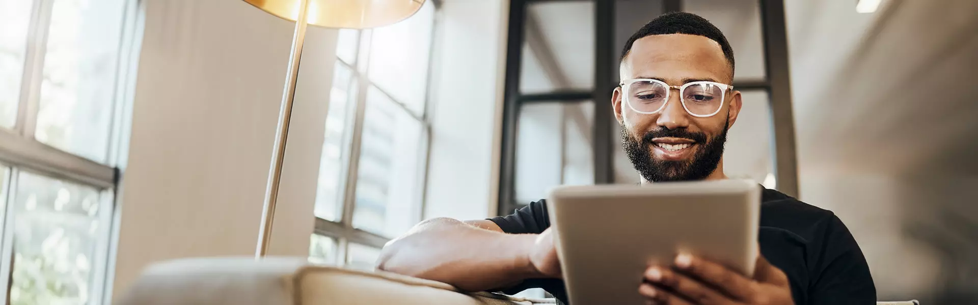 Sportlicher Mann Mitte 30 mit modischer Brille tippt auf Tablet 